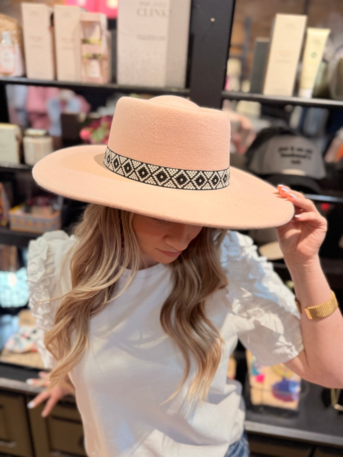 A person wearing a pink felt fedora hat with a boho-inspired pattern band.