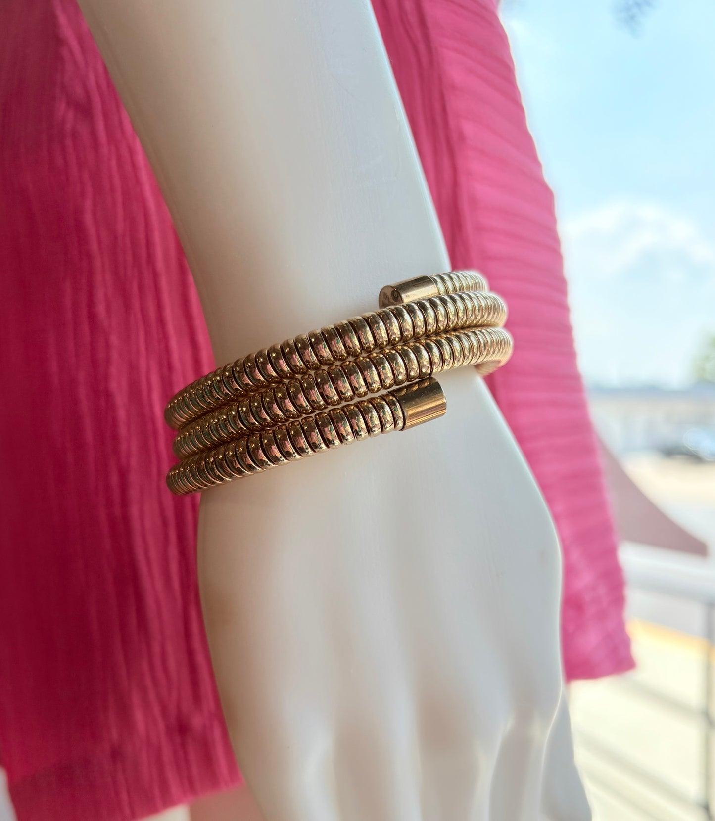 Close-up of a person wearing a stack of gold bracelets with a blurred outdoor background.