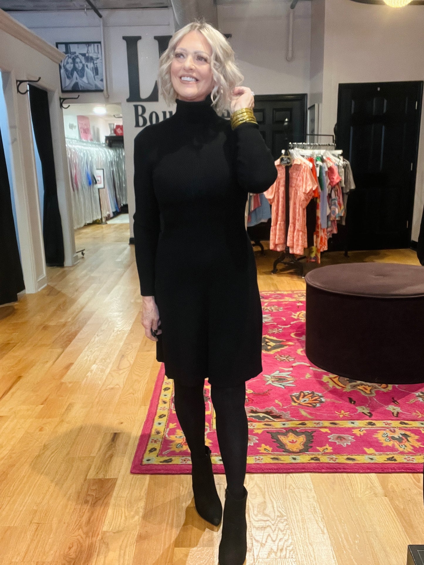 Woman in a black outfit standing in a clothing store with racks of clothes in the background.