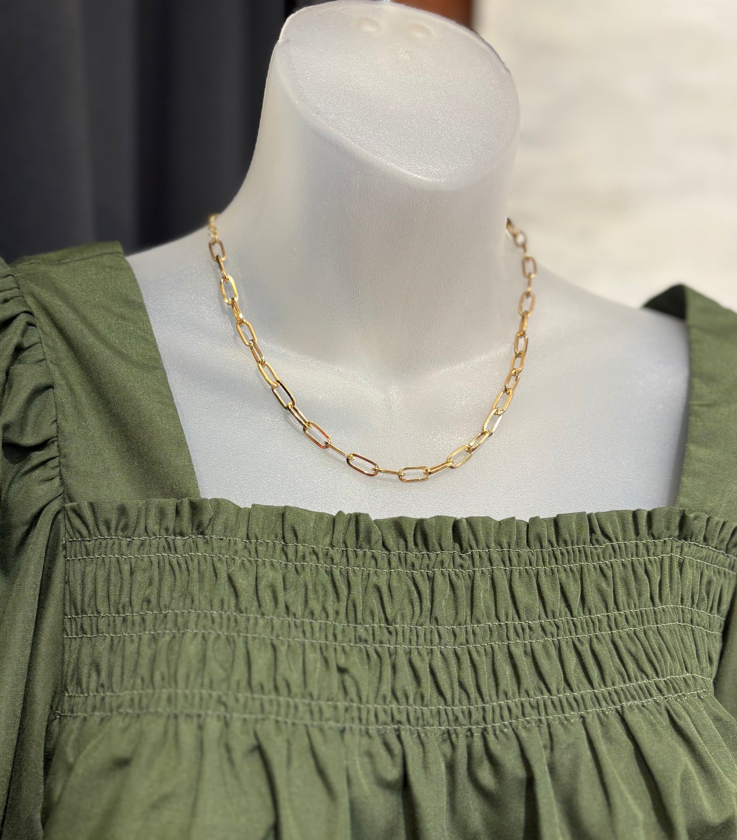 Mannequin wearing a green dress with a gold chain necklace against a neutral background