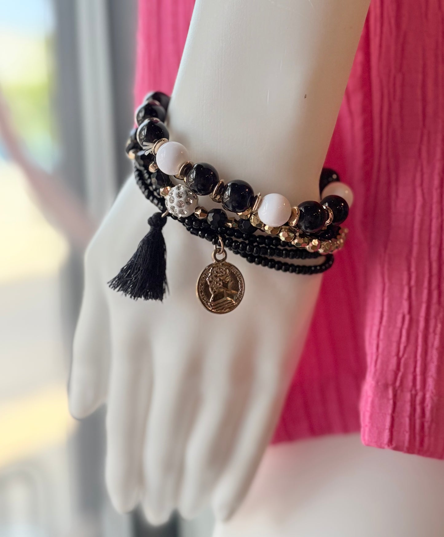 Multistrand beaded bracelet with tassels and a coin charm on a mannequin wrist.