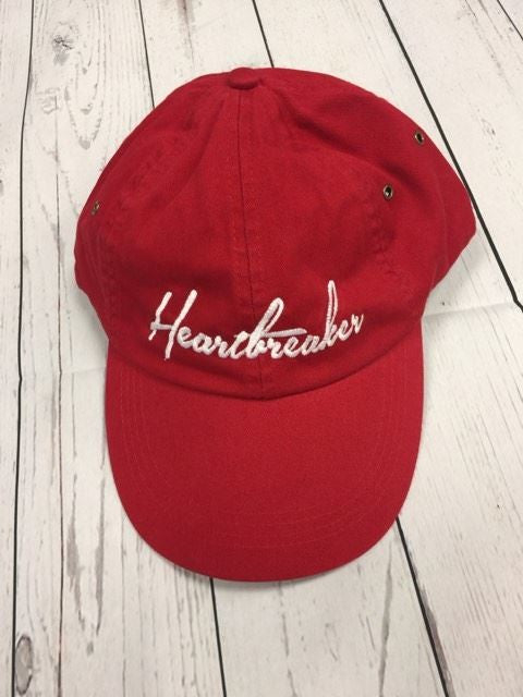 Red cap with 'Heartbreaker' text on a wooden surface