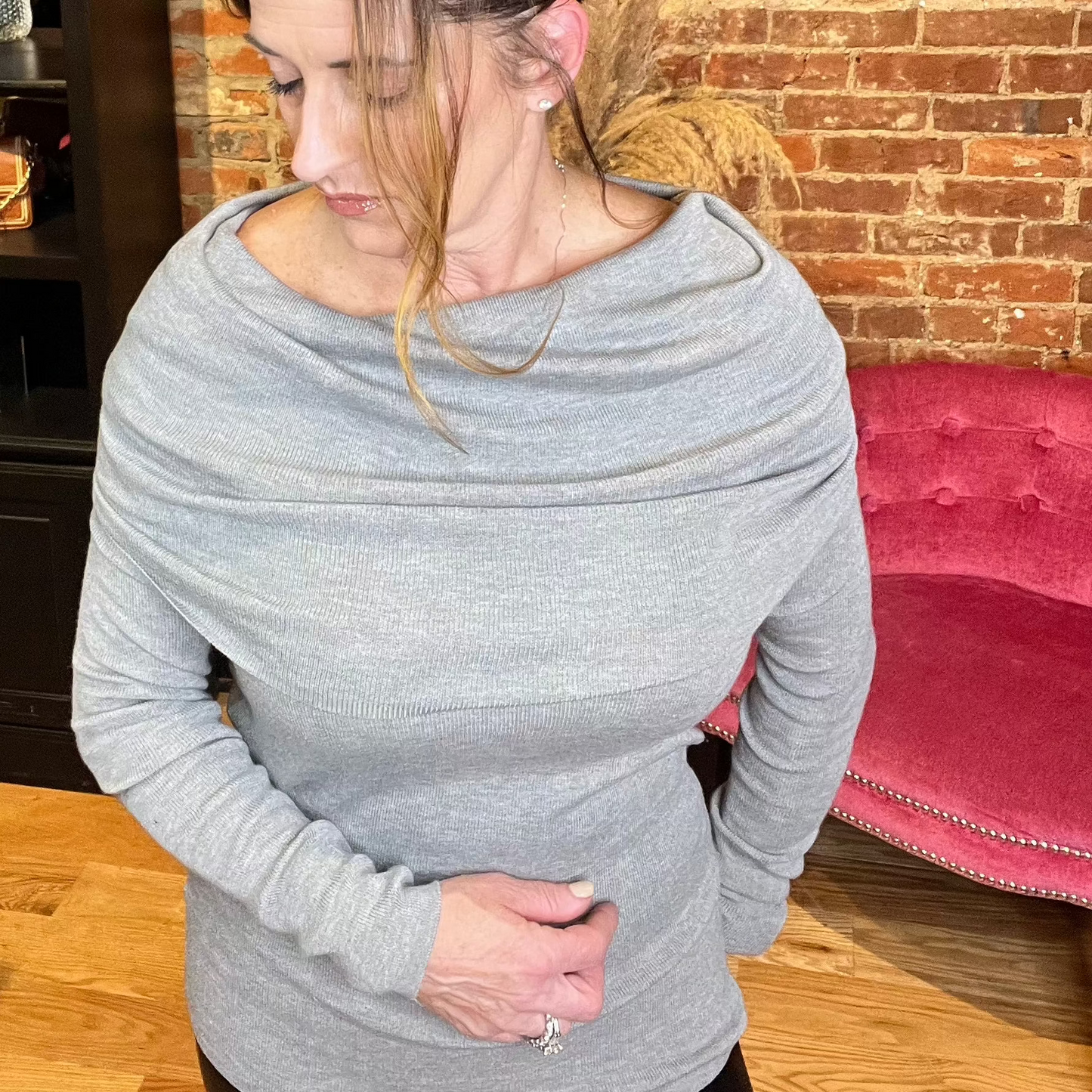A woman wearing an off-the-shoulder grey sweater top with long sleeves and a fold-over neckline, paired with black leggings.