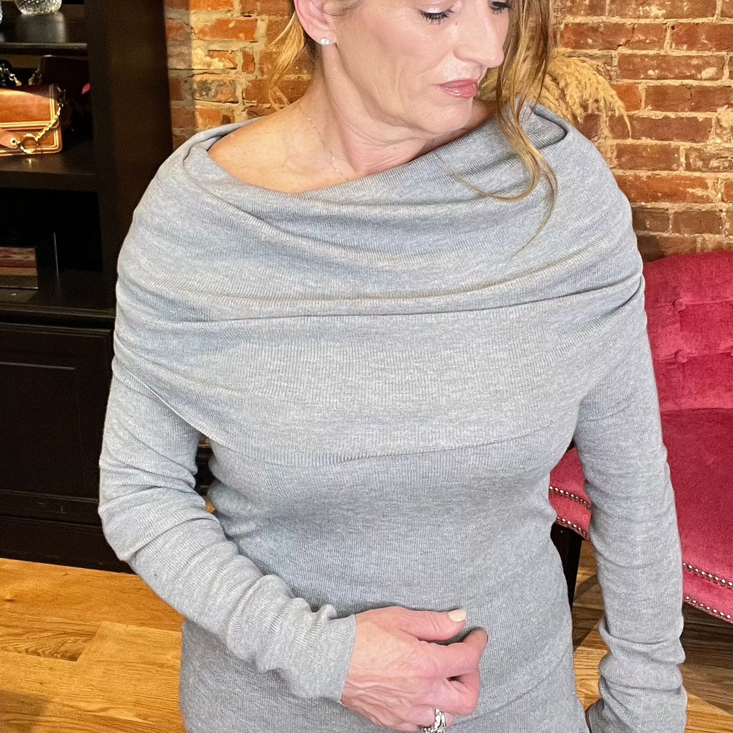 A woman wearing an off-the-shoulder black sweater top with long sleeves and a fold-over neckline, paired with black leggings.