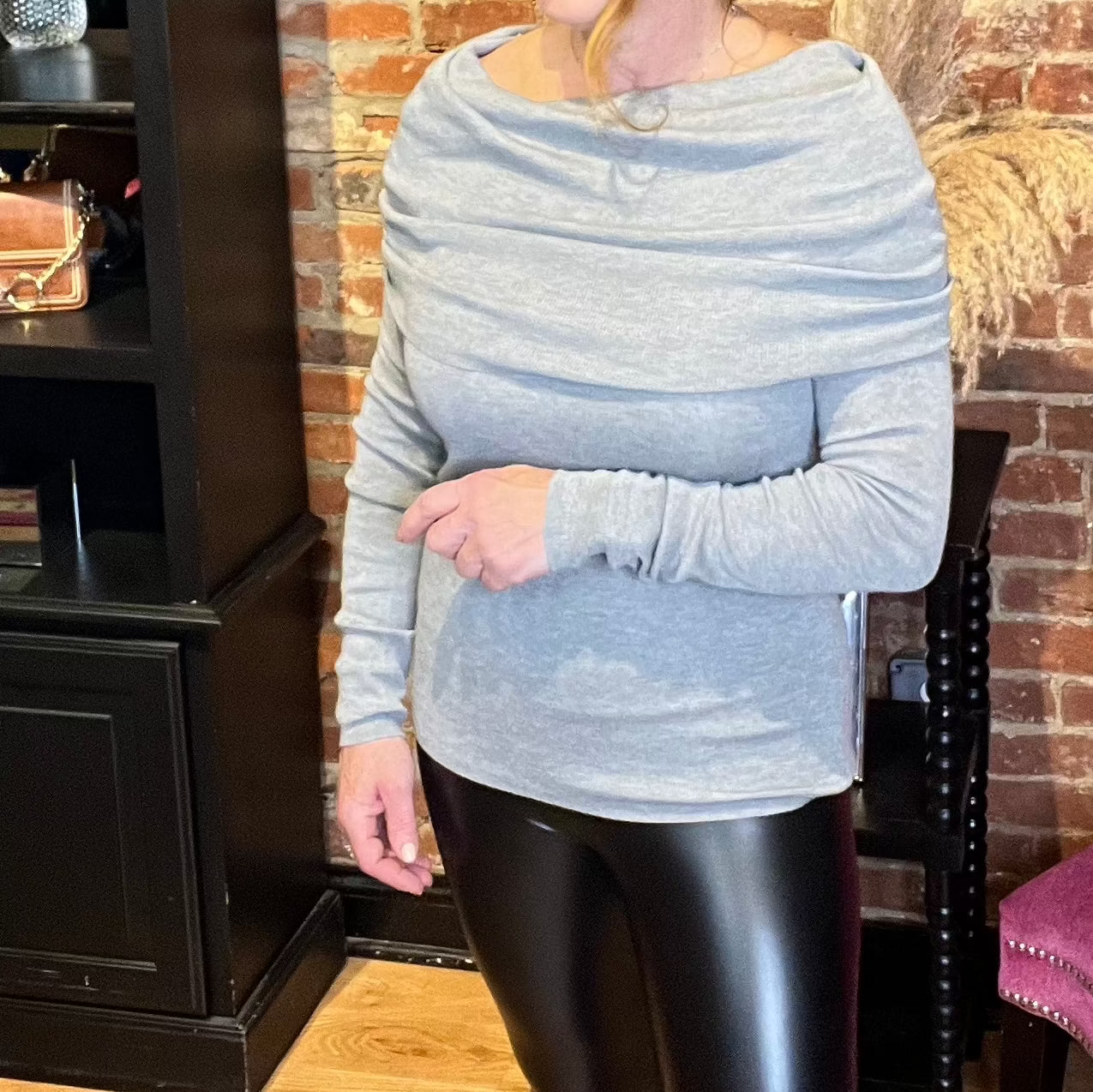 A woman wearing an off-the-shoulder grey sweater top with long sleeves and a fold-over neckline, paired with black leggings.