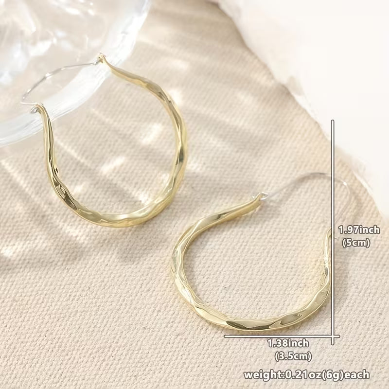 Gold-tone hammered hoop earrings displayed on a textured beige fabric background with a clear plastic bag edge visible. Measurement annotations show the earrings are approximately 1.