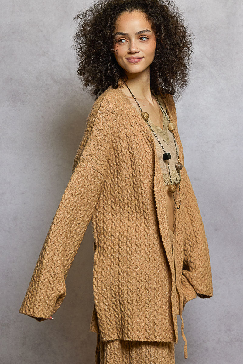 Woman wearing a beige knitted cardigan over a beige top against a gray background