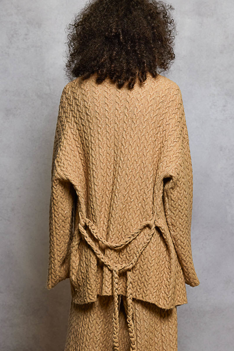 Person wearing a beige knitted outfit against a gray background