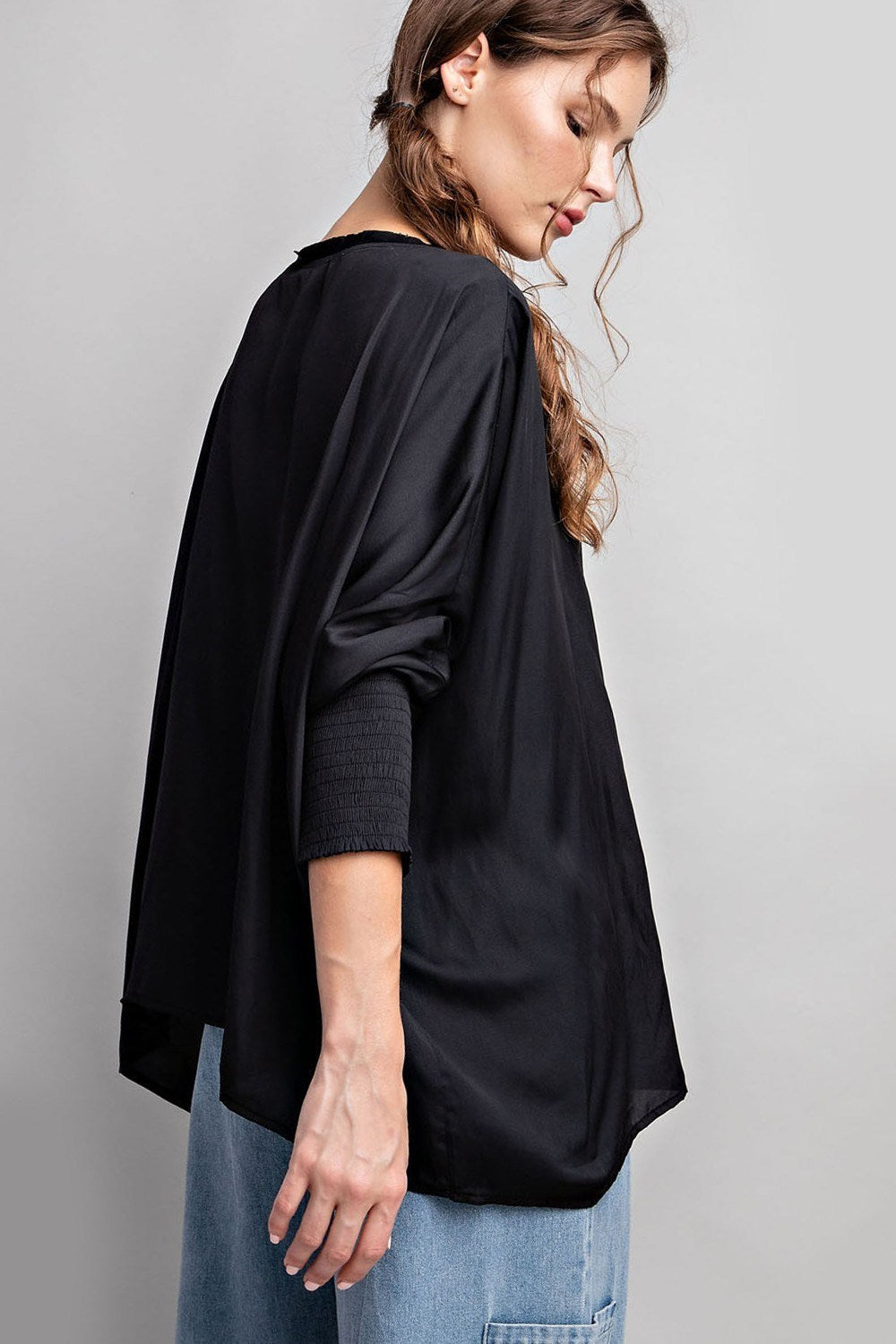 Woman wearing a black oversized top and blue jeans against a gray background