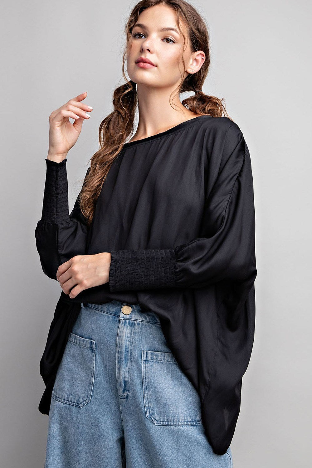 Woman wearing a black oversized shirt and blue jeans against a gray background