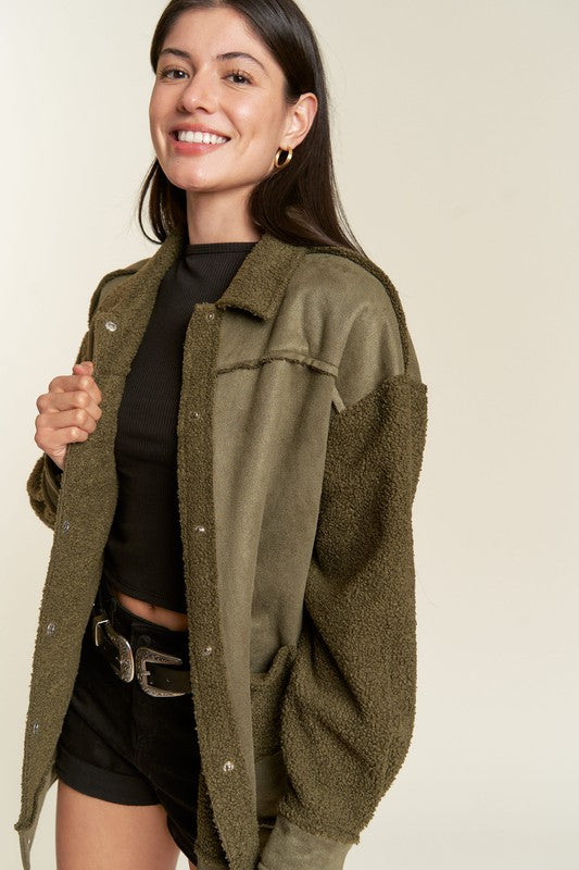 Woman wearing an olive green jacket over a black top and shorts on a beige background