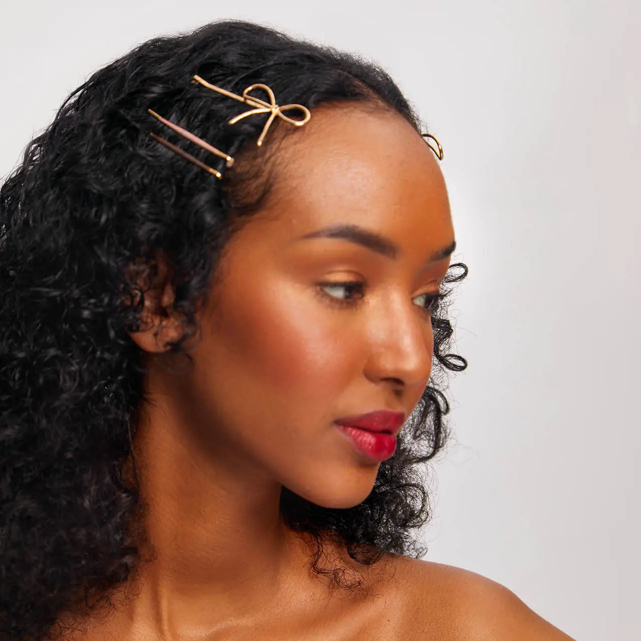 Woman with styled hair wearing a gold bow hair clip against a neutral background