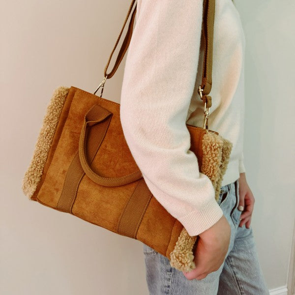 Person holding a brown suede handbag with shearling lining against a neutral background
