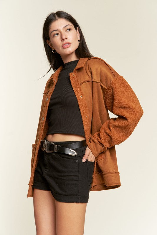 Woman wearing a brown jacket over a black top and shorts on a beige background