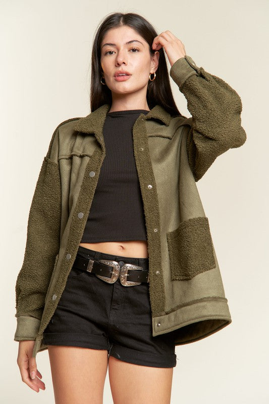 Woman wearing an olive green jacket over a black top and shorts on a beige background