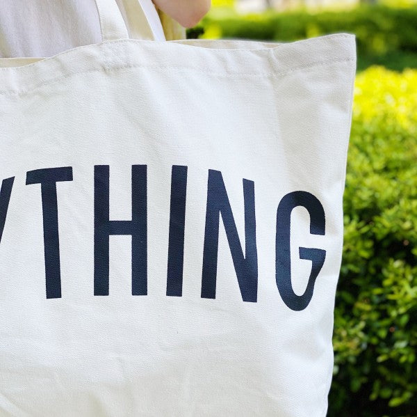 Tote bag with 'YTHING' printed on it held by a person outdoors.