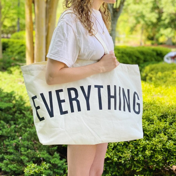 Person holding a tote bag with 'EVERYTHING' printed on it in an outdoor setting