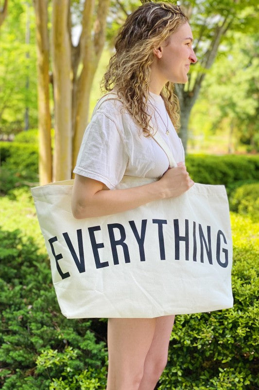 Person holding a tote bag with 'EVERYTHING' printed on it outdoors.
