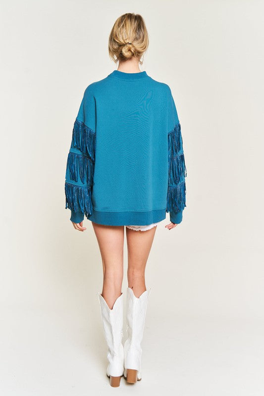 Person wearing a teal sweater with fringe details on a white background