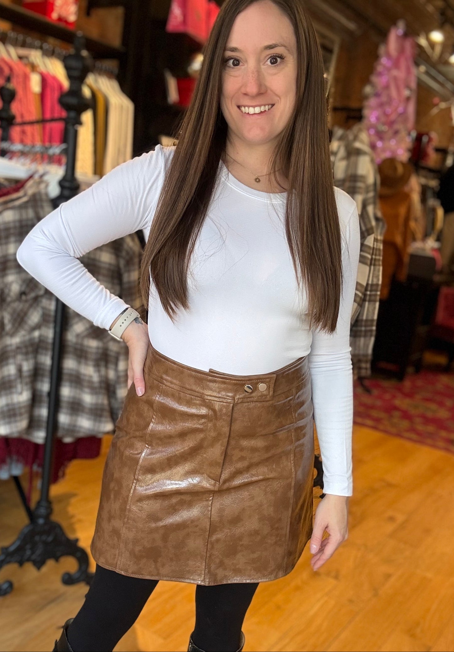 Woman wearing a white long-sleeve top and brown leather skirt in a clothing store.