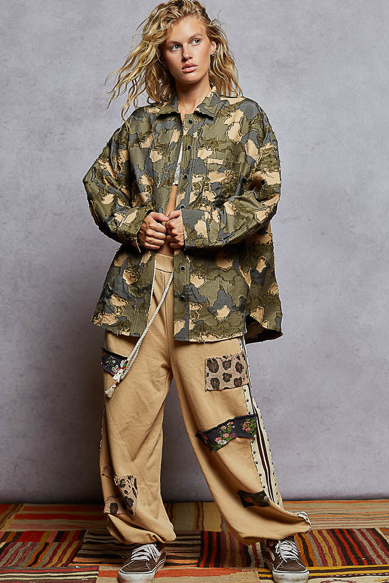 Person wearing a camouflage jacket and beige pants with leopard print accents on a gray background