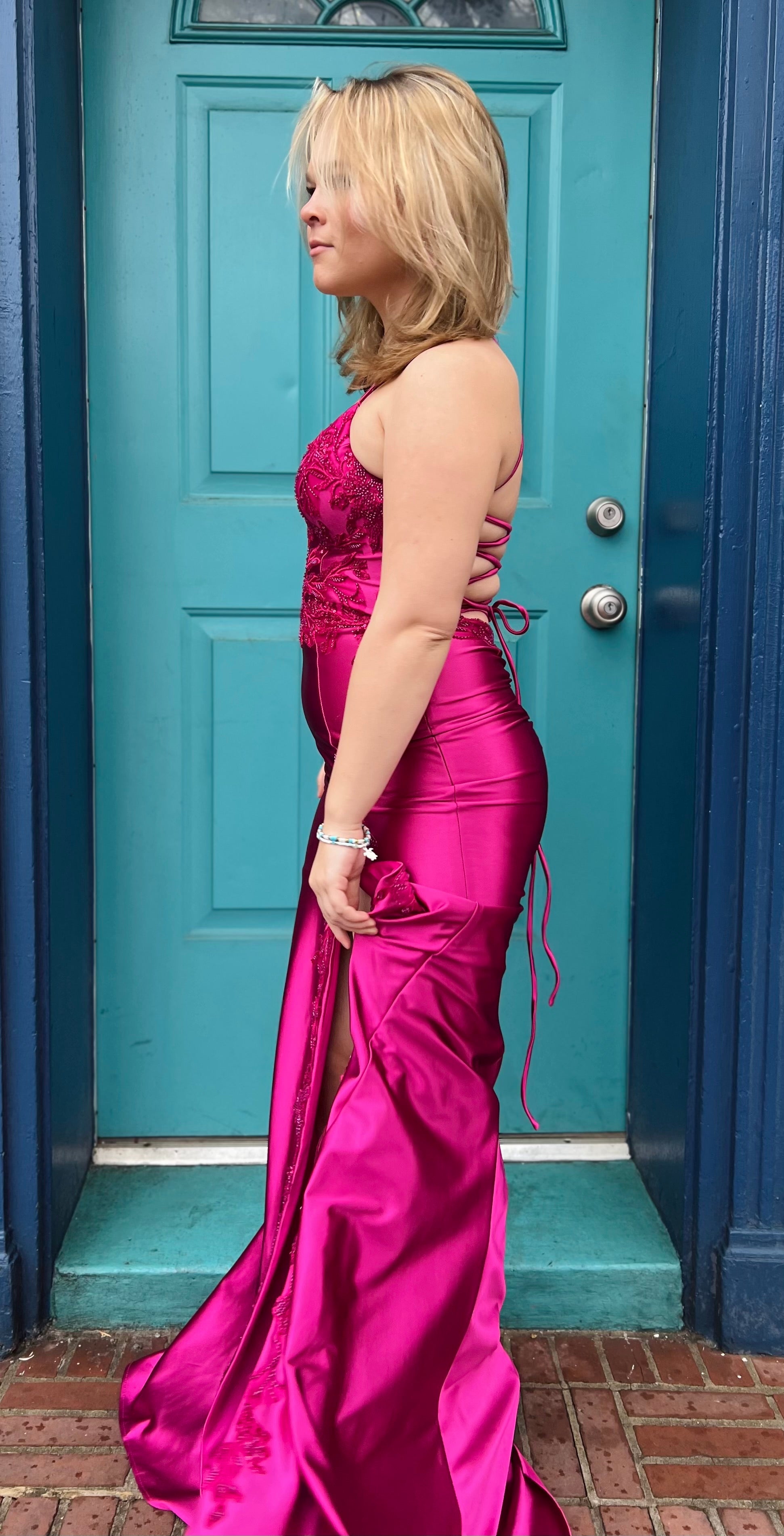 A woman modeling a Faviana Prom 11010 dress, featuring a V-neck, beaded bustier, leg slit, and lace-up back, in a grassy outdoor setting.