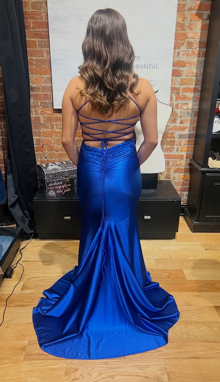 Woman wearing a blue evening gown with a lace-up back in a room with brick walls.
