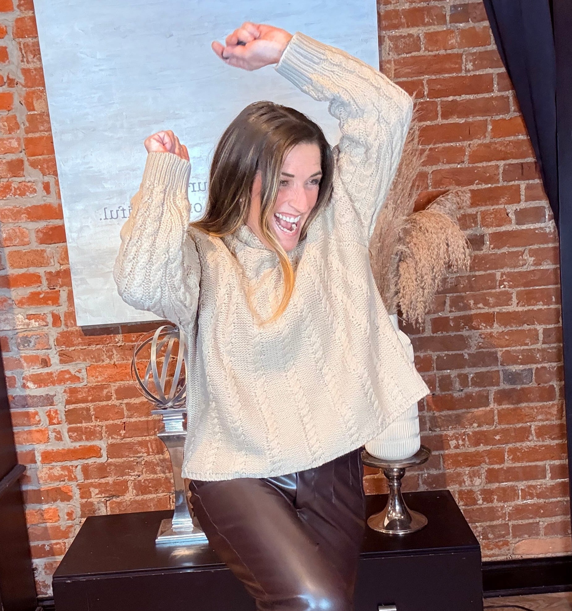 Person wearing a white sweater and brown boots standing on a rug with a brick wall background