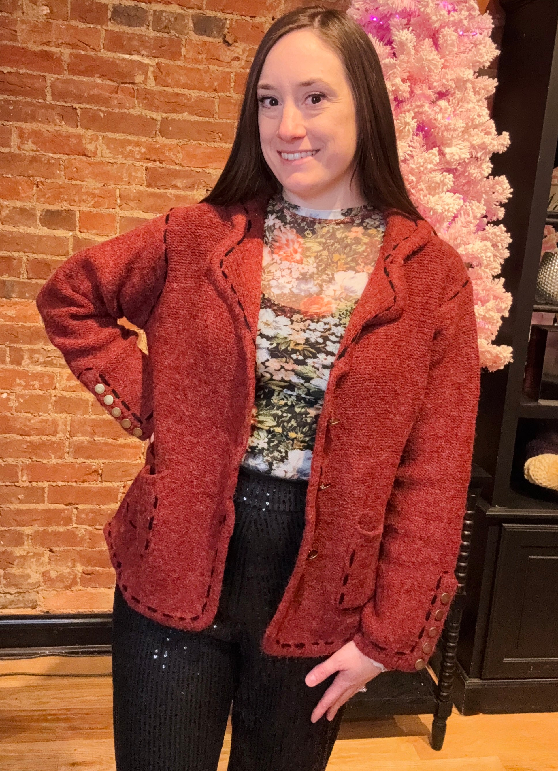 A woman wearing a red blazer with a classic pattern, featuring long sleeves, stitch detailing, lightly padded shoulders, and decorative gold buttons.