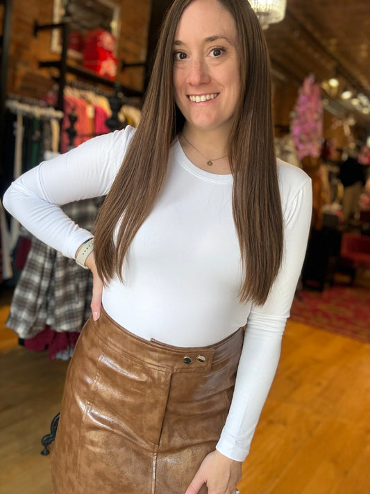 Woman wearing a white long-sleeve top and brown leather skirt in a store setting.