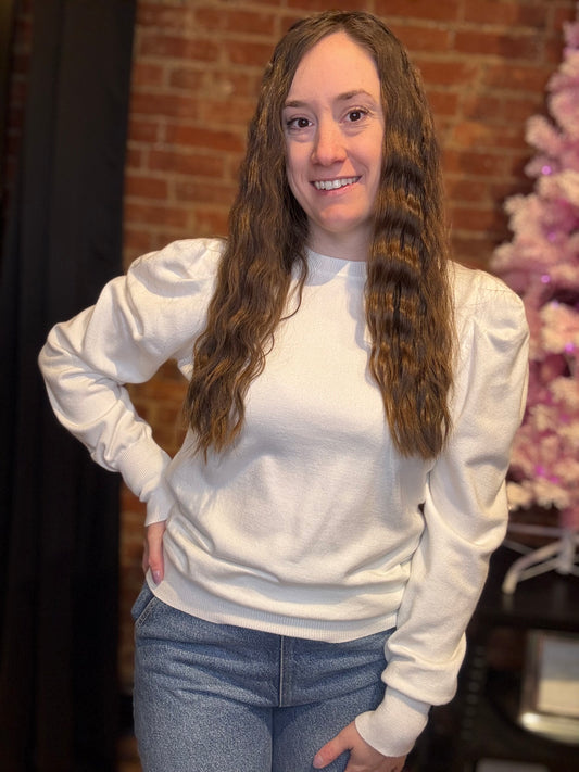 A woman wearing a black puff sleeve sweater top with black pants, accessorized with multiple bracelets and earrings.