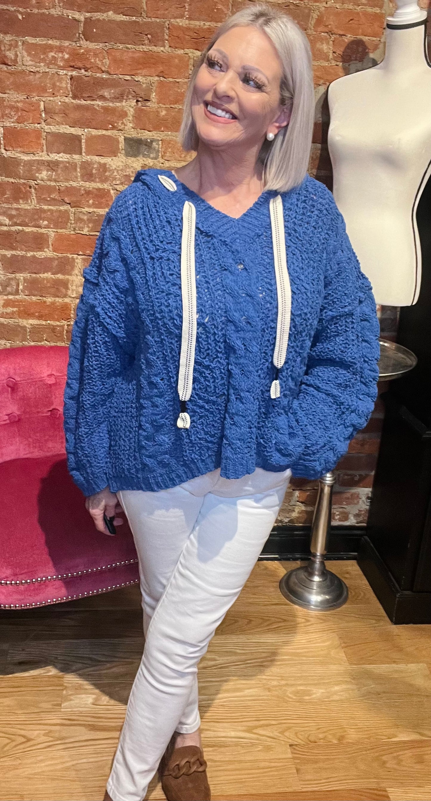 A woman smiling and wearing a white cozy pullover sweater with a v-neckline and long sleeves, paired with jeans.