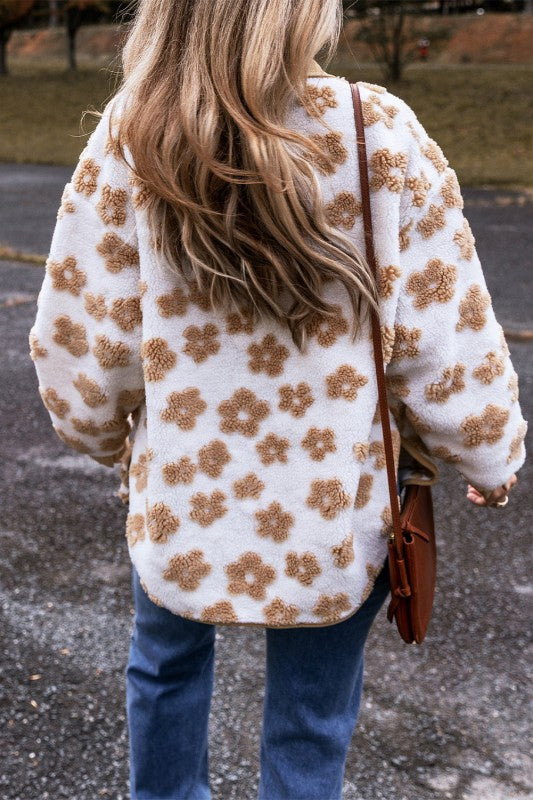 Person wearing a white floral-patterned coat with blue jeans and a brown bag.