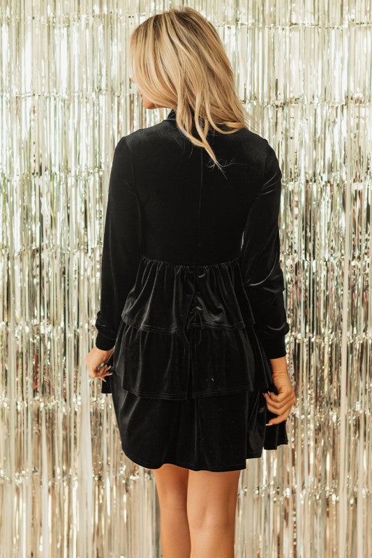 Person wearing a black dress with long sleeves against a silver tinsel background