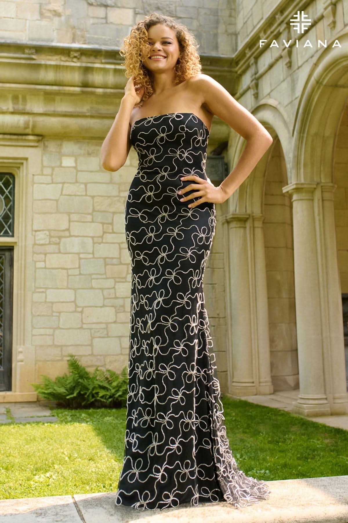 Woman in a strapless black evening gown with white patterns standing in front of a stone building.