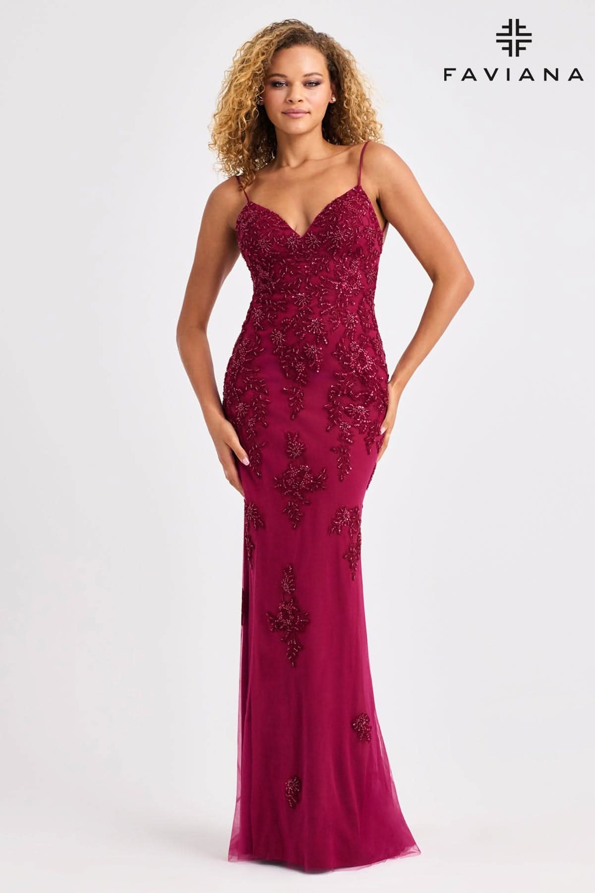Woman wearing a burgundy evening gown with floral embellishments on a white background, branded 'Faviana'.
