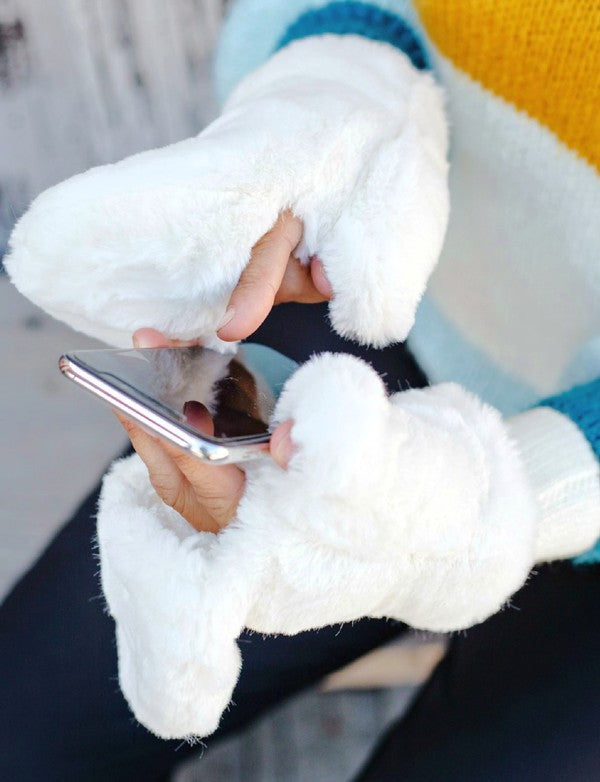 Person wearing white fuzzy gloves holding a phone with a blurred background