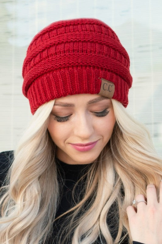 A woman wearing a red slouchy cable knit beanie hat with a visible brand tag on the brim.
