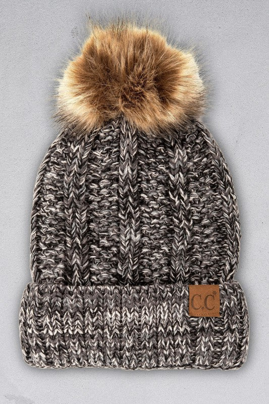 Knitted beanie with a fur pom-pom on a gray background