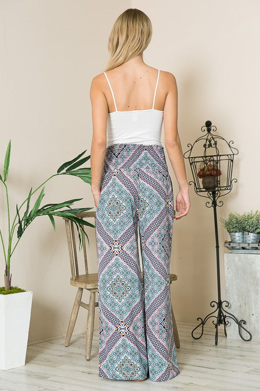 Woman wearing a white top and patterned pants standing in a room with decor elements.