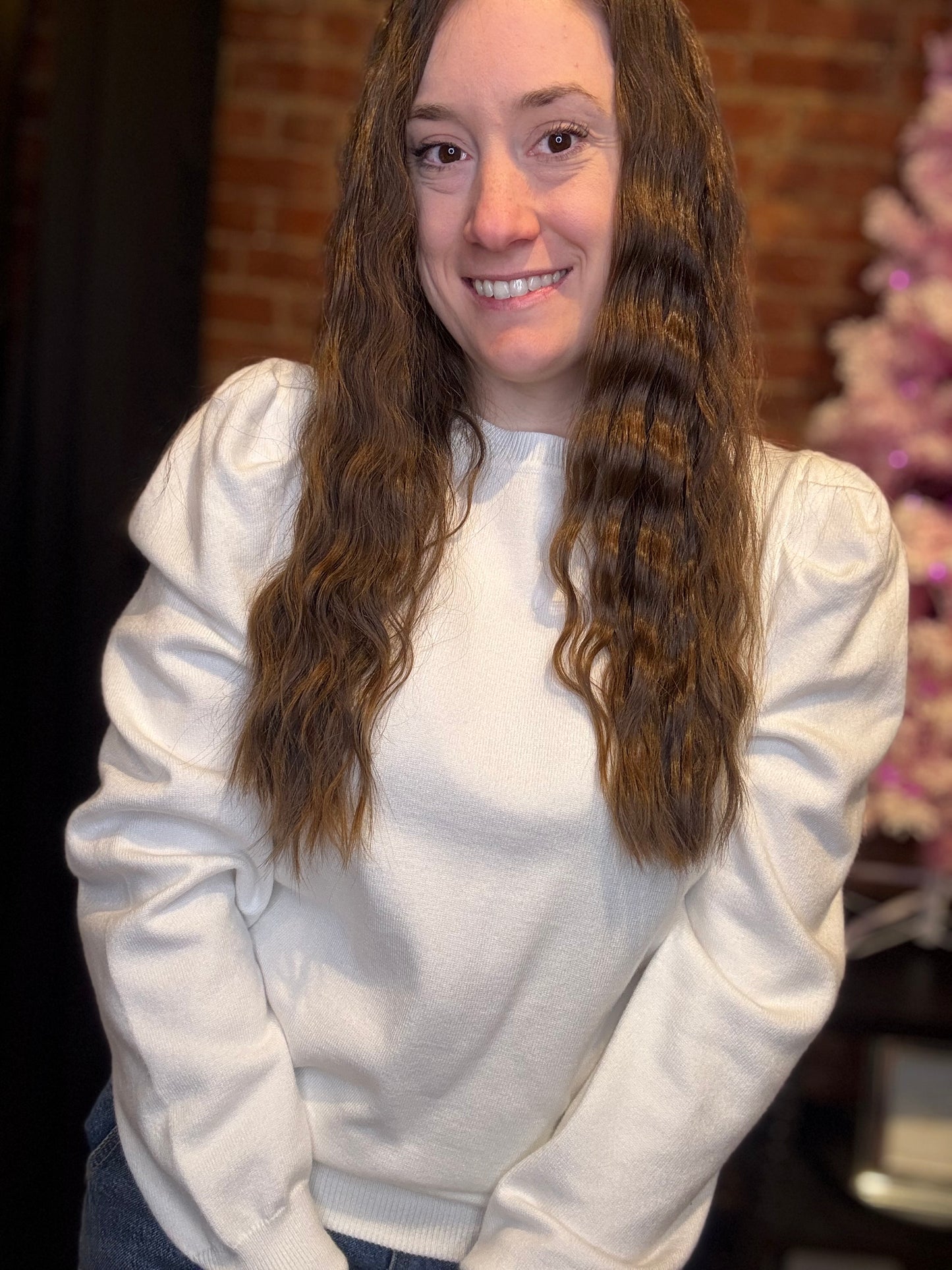 A woman wearing a black puff sleeve sweater top with black pants, accessorized with multiple bracelets and earrings.