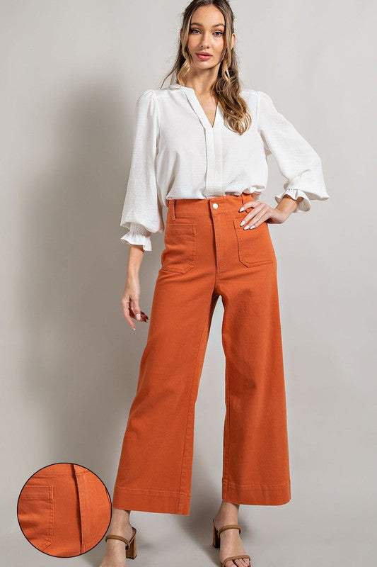 Woman wearing a white blouse and orange pants against a plain background