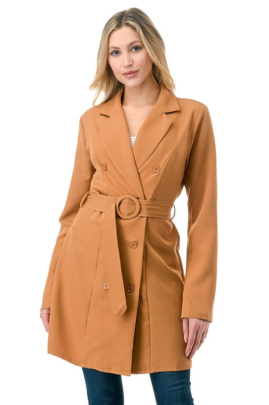 Woman wearing a tan coat with a belt on a white background