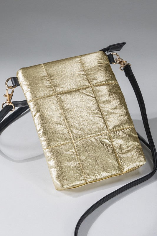 A metallic gold crossbody bag with a quilted design, featuring a faux leather strap and zipper closure, held by a person wearing blue jeans.