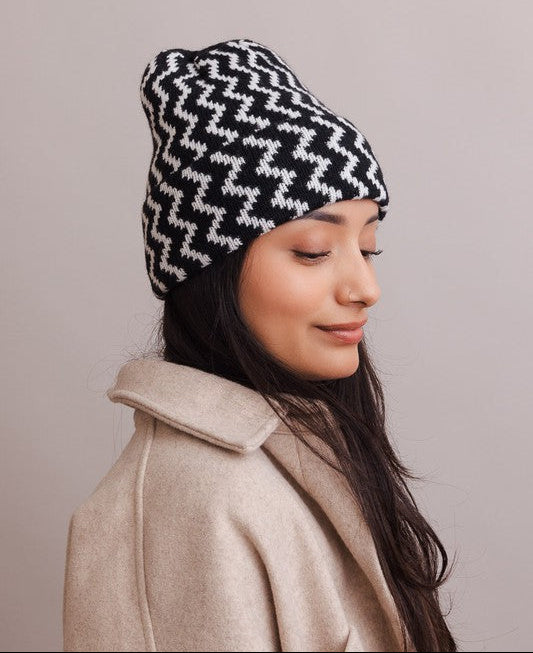 Woman wearing a black and white patterned beanie and beige coat against a plain background