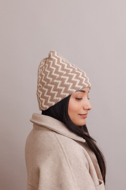 Woman wearing a beige and white patterned knit hat against a plain background