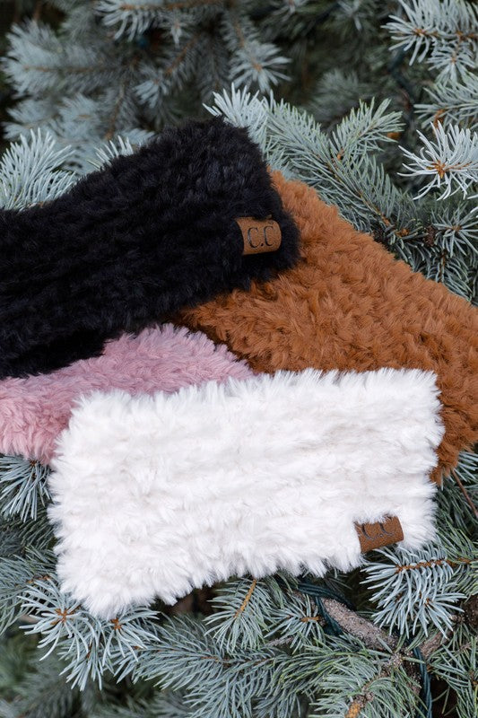 Four knitted headbands in black, brown, pink, and white on a pine branch.