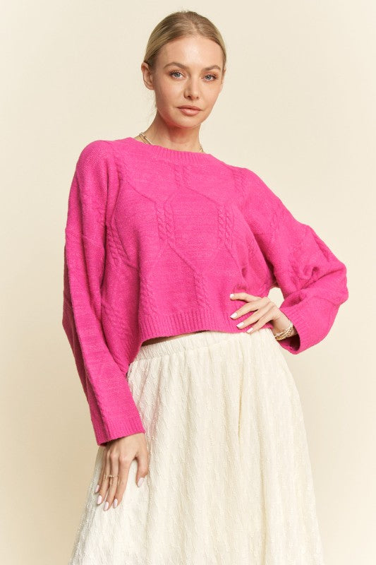 Woman wearing a bright pink sweater and white pants on a beige background