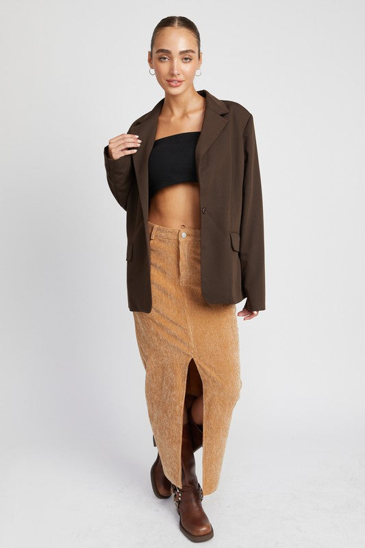 Woman wearing a brown coat, black top, and tan skirt on a white background