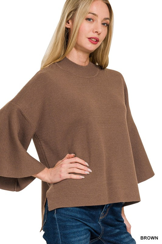 Woman wearing a brown bell sleeve sweater top with blue denim jeans with a white background